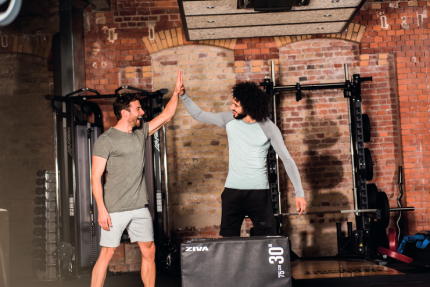 Zwei junge Männer im Fitnessstudio klatschen sich ab.