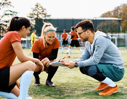 Trainer spricht mit zwei Athletinnen, alle in der Hocke